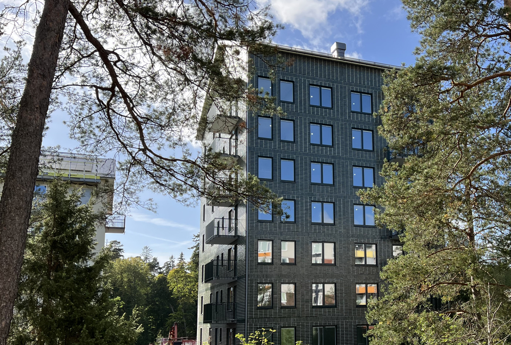 Ett grönt flerbostadshus i sju våningar med träd i förgrunden.