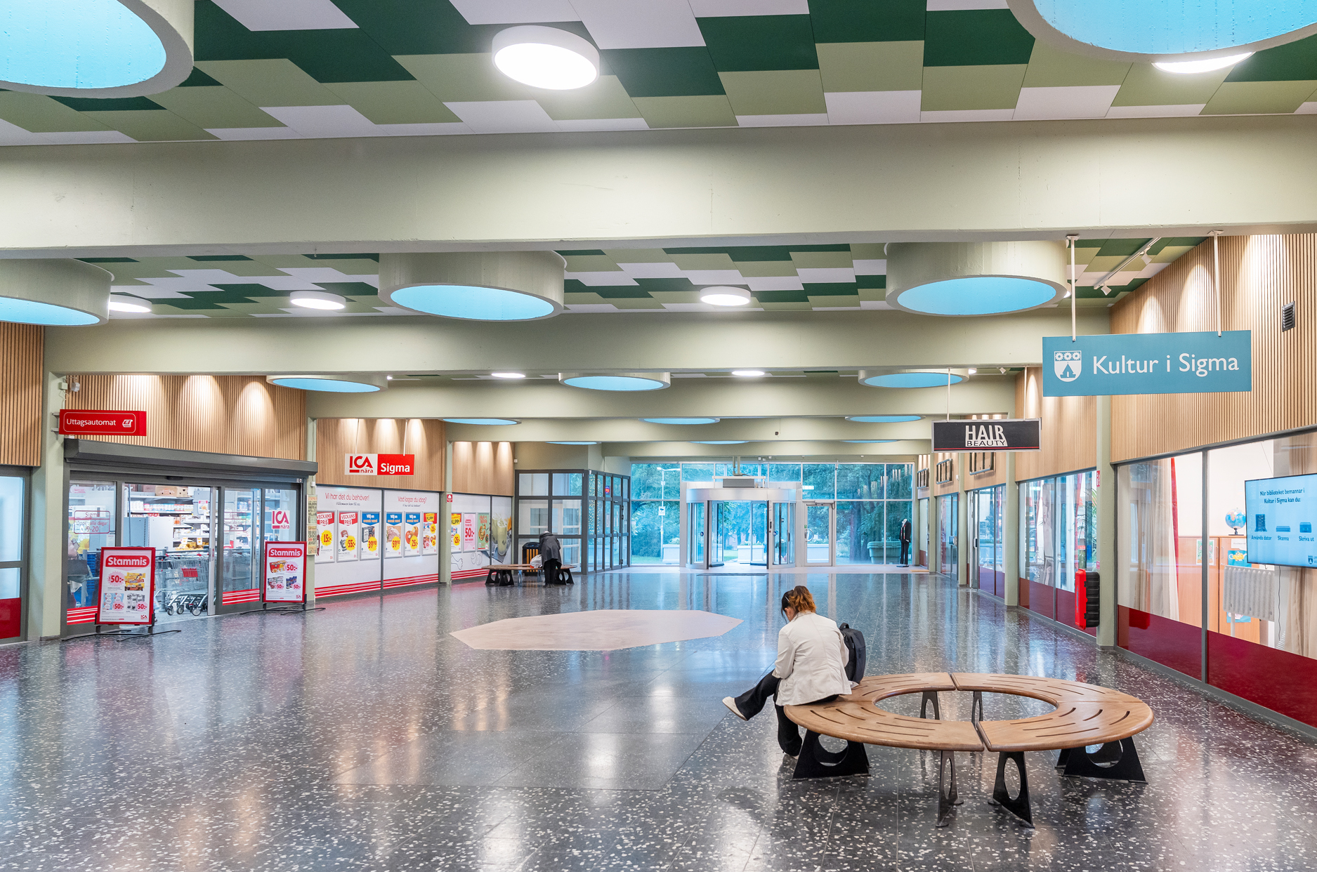Interiör av inomhuscentrum med en rund sittplats där det sitter en person med ryggen mot fotografen.
