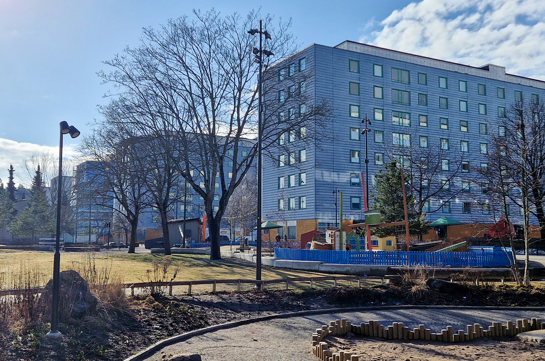 Blå byggnader på rad med park i förgrunden.